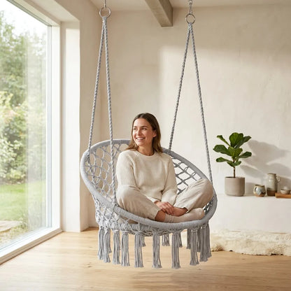 Fauteuil suspendu ovale en filet tressé gris, franges, personne assise.