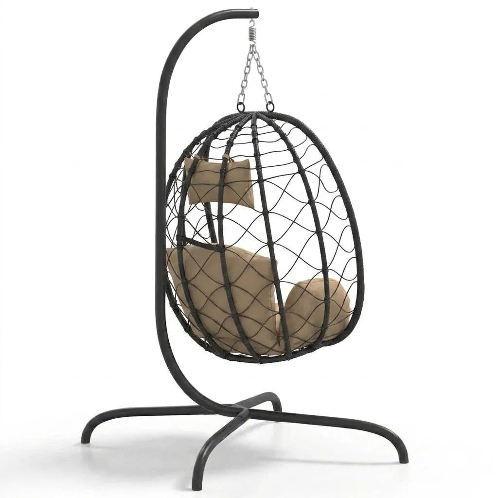 Fauteuil suspendu en rotin noir, coussins beige et attache en chaîne au sommet.