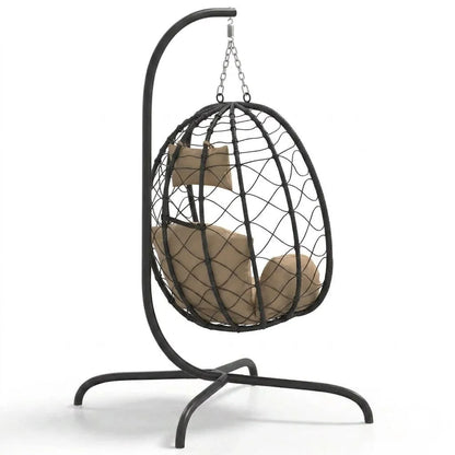 Fauteuil suspendu en rotin noir, coussins beige et attache en chaîne au sommet.