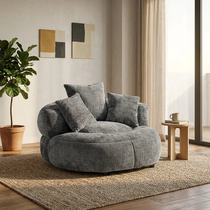 Fauteuil rond en tissu gris avec dossier haut et trois coussins, assise profonde.